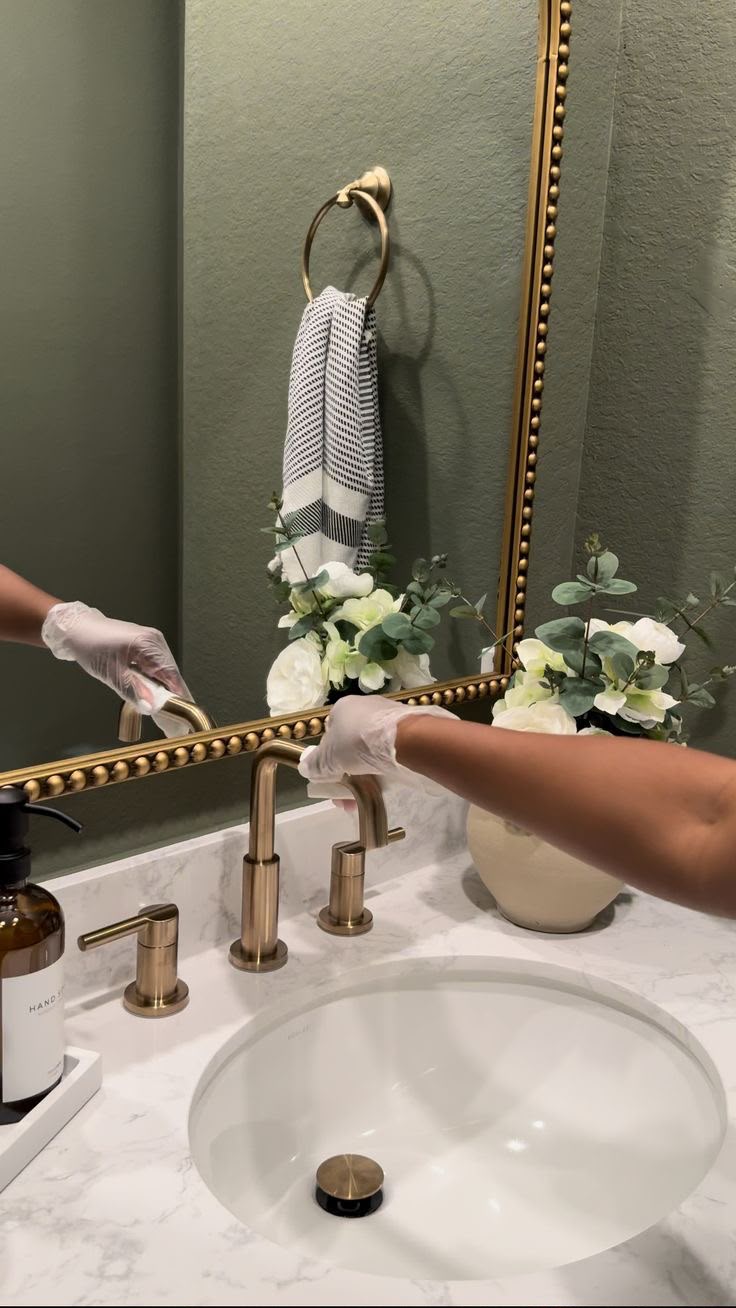 Cleaner sanitising a bathroom sink and gold fixtures